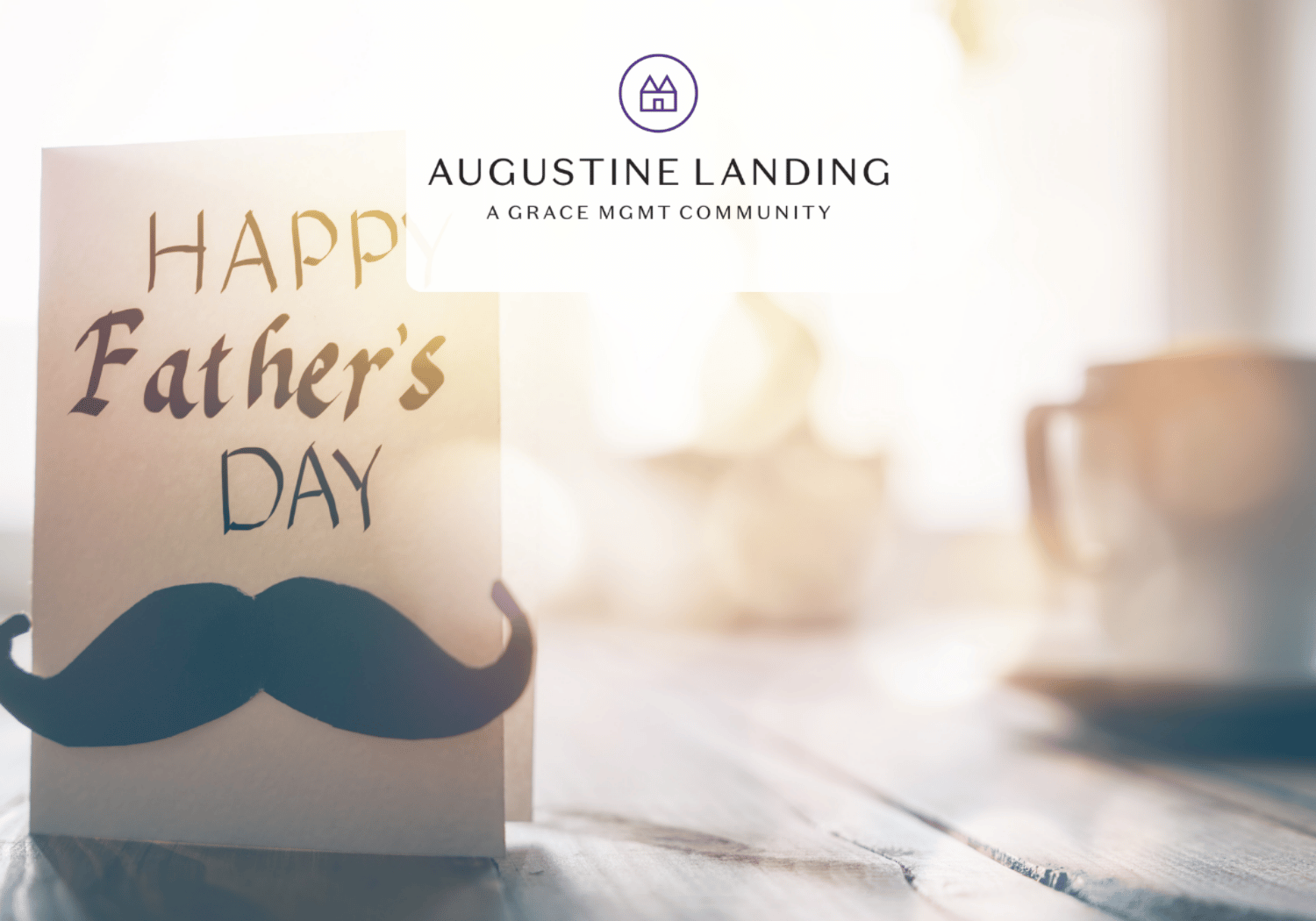 Father's Day greeting card with a dark mustache cutout on a wooden table; blurred mug in the warm background; Augustine Landing logo above.