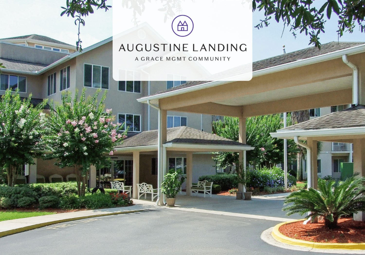 Entrance to Augustine Landing senior living campus with a covered drop-off, seating area, and well-kept landscaping beneath a translucent logo that reads 'AUGUSTINE LANDING A GRACE MGMT COMMUNITY'